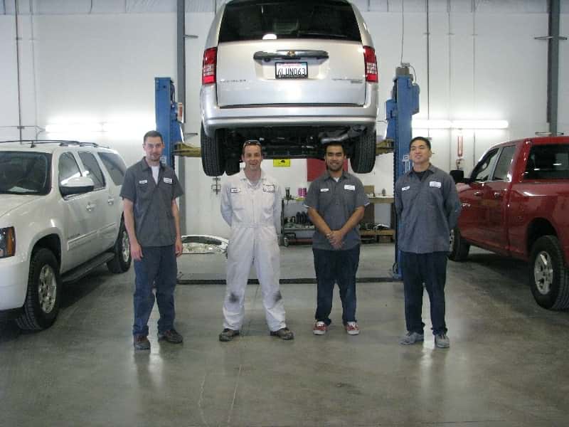 Collision Specialists Standing Under Vehicle on Lift